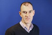 Image of Garry Haines wearing a blue jumper in front of a dark blue background